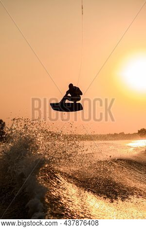 Silhouette Of Active Man Making Trick With Wakeboard On Bright Orange Sky And Sun Background.