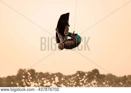 Man Makes Extreme Stunts Jumping And Flips On Wakeboard Against Sky Background.