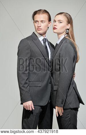 Fashion shot of stylish fashion models young man and pretty woman posing in elegant striped pantsuits on a grey studio background. Impeccable look. Men's clothing style.