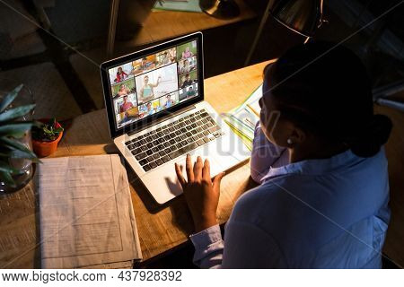 African american woman using laptop for video call, with diverse elementary school pupils on screen. communication technology and online education, digital composite image.