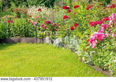 A Part Of The Garden Area With A Variety Of Blooming Flowers And A Well-tended Green Lawn.