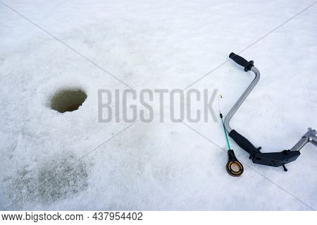 Winter Fishing. An Ice Screw And A Fishing Rod Lie On The Ice Next To The Drilled Hole. Copy Space