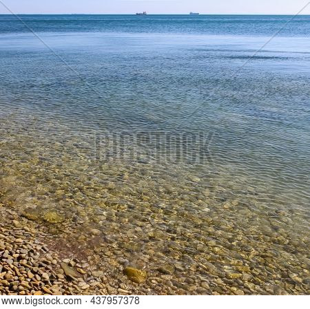 A Rocky Beach And On The Sea Level Horizon Ships Dispersed Under A Blue Sky