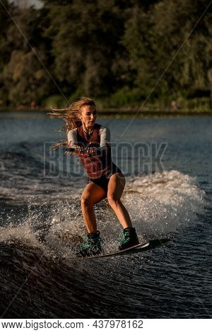 Handsome Woman Holds Rope And Jumping With Wakeboard Over River Wave.