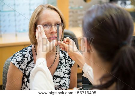 Female optician measuring mature woman's eyeglasses in store