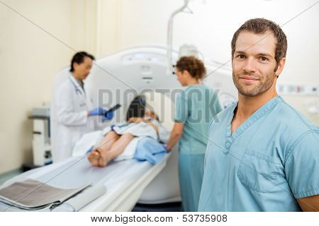 Portrait of male nurse with colleague and radiologist preparing patient for CT scan in examination room