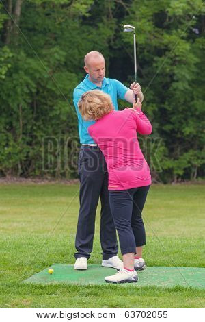 A lady golfer being taught to play golf by a Pro on a practice driving range.