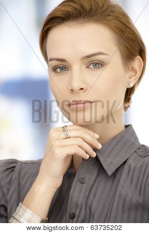 Portrait of attractive thinking businesswoman looking at camera, hand on chin.