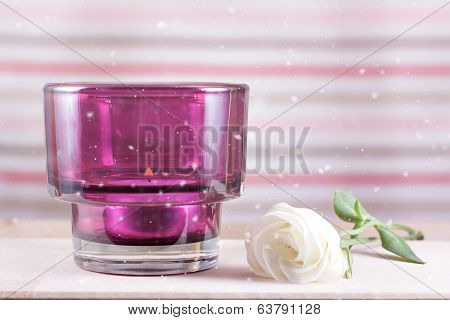 Candle on wooden table with flowers and snowfalling