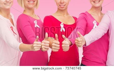 healthcare, people, gesture and medicine concept - close up of smiling women in blank shirts with breast cancer awareness ribbons showing thumbs up over pink background