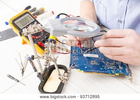 Serviceman checks PCB with a digital multimeter in the service workshop
