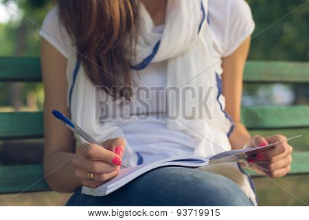 Young Woman Student Sitting On A Bench In The Park