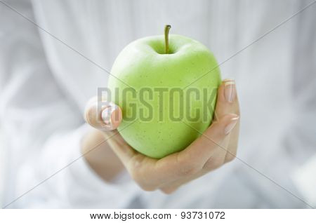 Closeup shot of a woman holding healthy green apple. Girl with a green apple in hands. Shallow depth of field with focus on the green apple.
