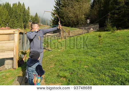 Father and son shoot arrows at a target.