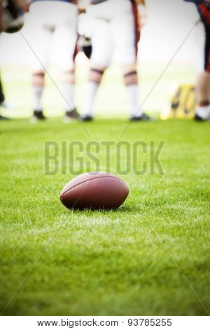Close up of an american football on the field, players in the background