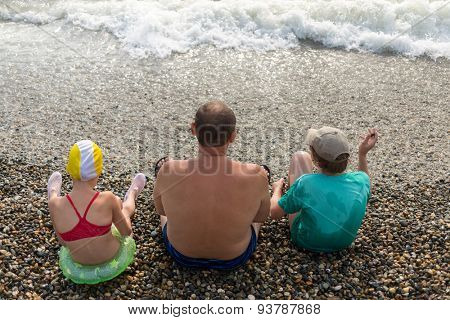 grandfather with grandchildren sit on the beach and look at the sea