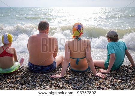 family of four sitting on a pebble beach
