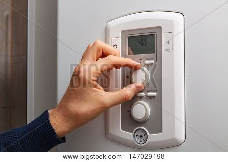 Men hand regulate low temperature on 40 degree in control panel of central heating.