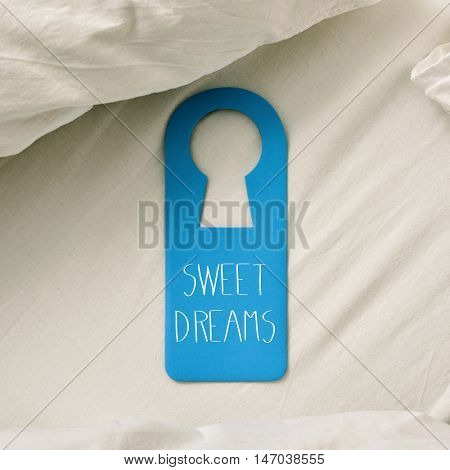 closeup of a blue door hanger with the text sweet dreams written in it, placed on a comfortable bed