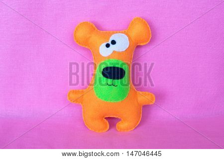 Orange felt toy bear on pink background
