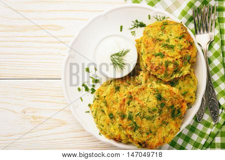 Fritters with zucchini and carrots on white wooden background.