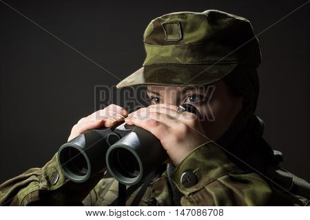 Portrait of unarmed woman with camouflage. Young female soldier observe with binoculars. War military army people concept