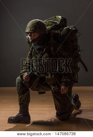 Unarmed woman with camouflage on one knee. Young female soldier observe with binoculars and backpack. War military army people concept