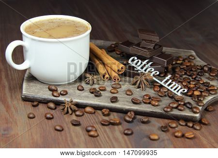 cup of coffee with chocolate, coffee grains, an anisetree, cinnamon and the inscription coffee time