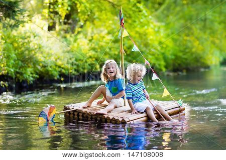 Two children on wooden raft catching fish with a colorful net in a river and playing with water on hot summer day. Outdoor fun and adventure for kids. Boy and girl in toy boat. Sailor role game.