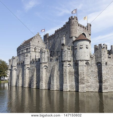 castle Gravensteen in the Beldian city of Ghent with reflection in in river and blue sky