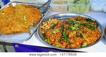 Southern Thai spicy pasta and noodles, with fresh sprouts, cucumbers, and greens on metal platters, for sale in Ranot, Thailand