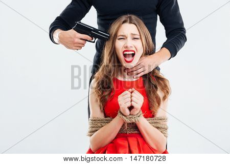 Woman sitting bounded with ropes and shouting threatened by man with gun