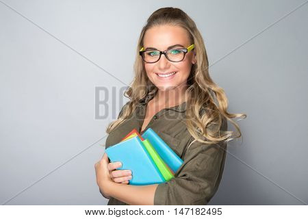 Portrait of a happy smiling student girl with colorful books in hands over gray background, enjoying education in high school