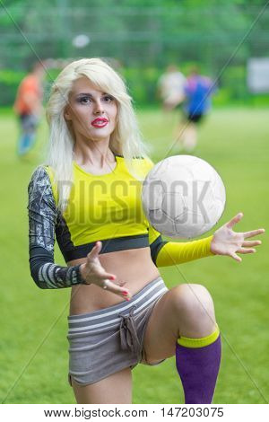 Beautiful woman plaing with ball in yellow shortened top on football field