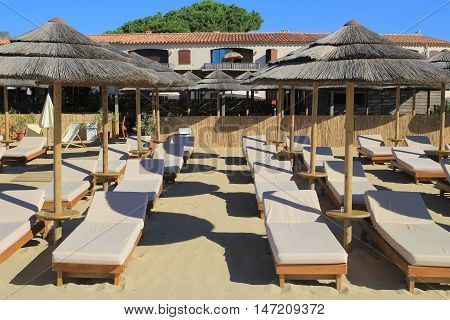 Wooden sun loungers with that umbrellas on the sand in front of a beach restaurant