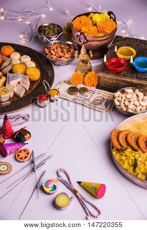 oil lamp or diya with crackers, sweet or mithai, dry fruits, indian currency notes, marigold flower and statue of Goddess Laxmi on diwali night while laxmi pujan or pooja