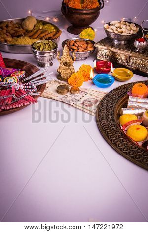 oil lamp or diya with crackers, sweet or mithai, dry fruits, indian currency notes, marigold flower and statue of Goddess Laxmi on diwali night while laxmi pujan or pooja