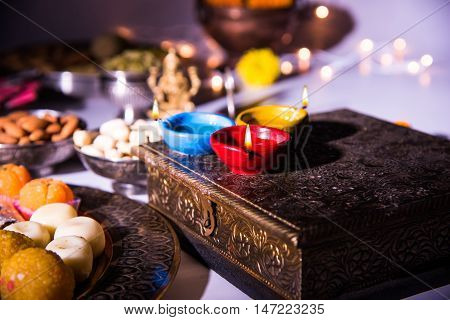 oil lamp or diya with crackers, sweet or mithai, dry fruits, indian currency notes, marigold flower and statue of Goddess Laxmi on diwali night while laxmi pujan or pooja