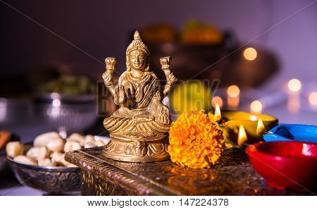 oil lamp or diya with crackers, sweet or mithai, dry fruits, indian currency notes, marigold flower and statue of Goddess Laxmi on diwali night while laxmi pujan or pooja