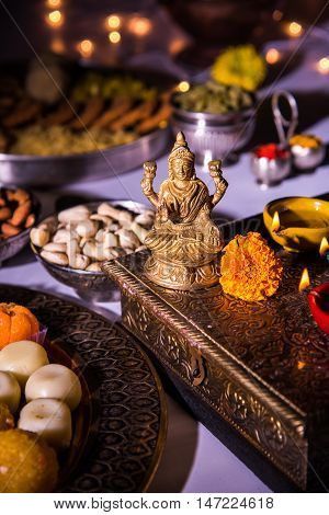 oil lamp or diya with crackers, sweet or mithai, dry fruits, indian currency notes, marigold flower and statue of Goddess Laxmi on diwali night while laxmi pujan or pooja