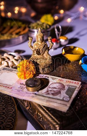 oil lamp or diya with crackers, sweet or mithai, dry fruits, indian currency notes, marigold flower and statue of Goddess Laxmi on diwali night while laxmi pujan or pooja