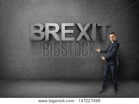 Businessman stands showing big 3d 'brexit' word by both hands on concrete background. British withdrawal. Euroscepticism. Unired Kingdom and European Union.