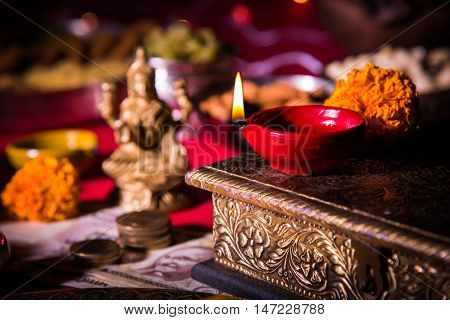 oil lamp or diya with crackers, sweet or mithai, dry fruits, indian currency notes, marigold flower and statue of Goddess Laxmi on diwali night