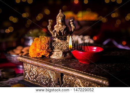 oil lamp or diya with crackers, sweet or mithai, dry fruits, indian currency notes, marigold flower and statue of Goddess Laxmi on diwali night
