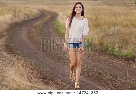 Young girl outdoors enjoying nature. She walking along the road in autumn field smiling happily. Selective focus warm tinted.