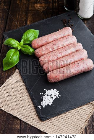Raw beef sausages with salt and basil on stone board.Dark brown board. Salt and pepper on background