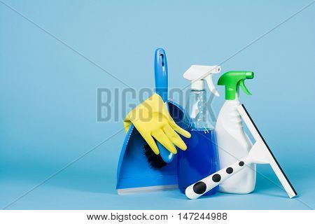 Cleaning concept - mixed detergents and cleaning accessories isolated on blue seamless background.
