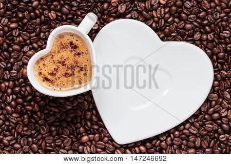 Hot beverage. White coffee cup heart shaped with cappucino latte on roasted beans background