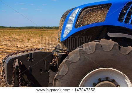 The front part of a blue tractor closeup. Agricultural machine standing in a field during plowing and harvesting soil.