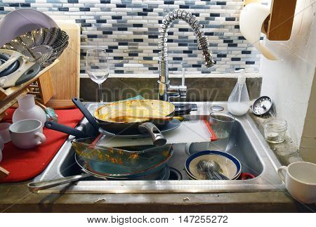 Dirty sink filled with dishes in a messy household kitchen
